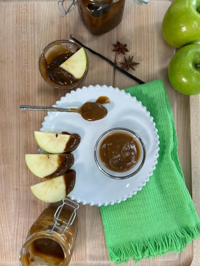 Green apple slices dipped in vegan caramel sauce with jars of caramel, a vanilla bean and star anise